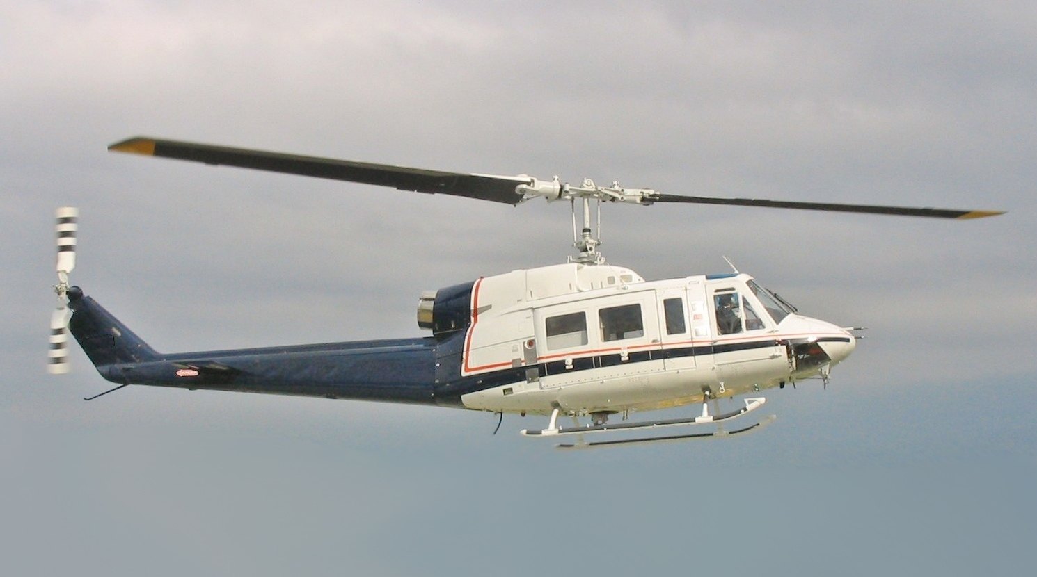 A Bell 214B in flight in white and dark blue livery, showing the type's single large exhaust duct and wide-chord main rotor blades