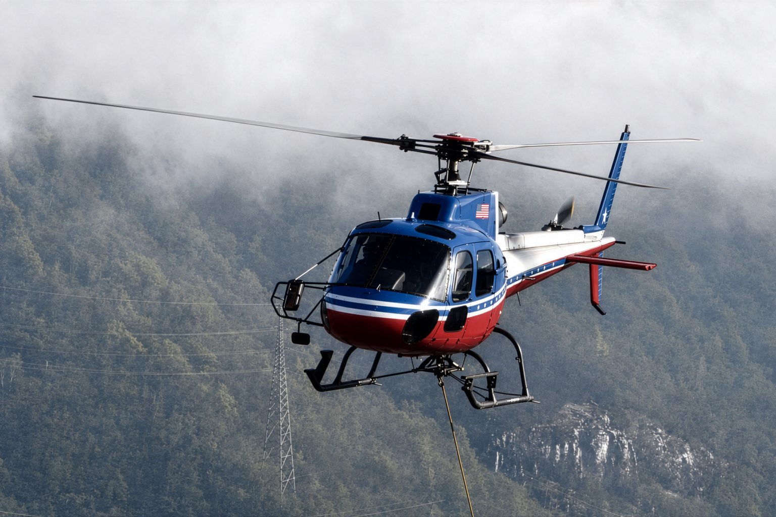 A heavy-lift helicopter working a longline pick above a rooftop structure, load suspended on a synthetic line with the flight path clear of surrounding buildings