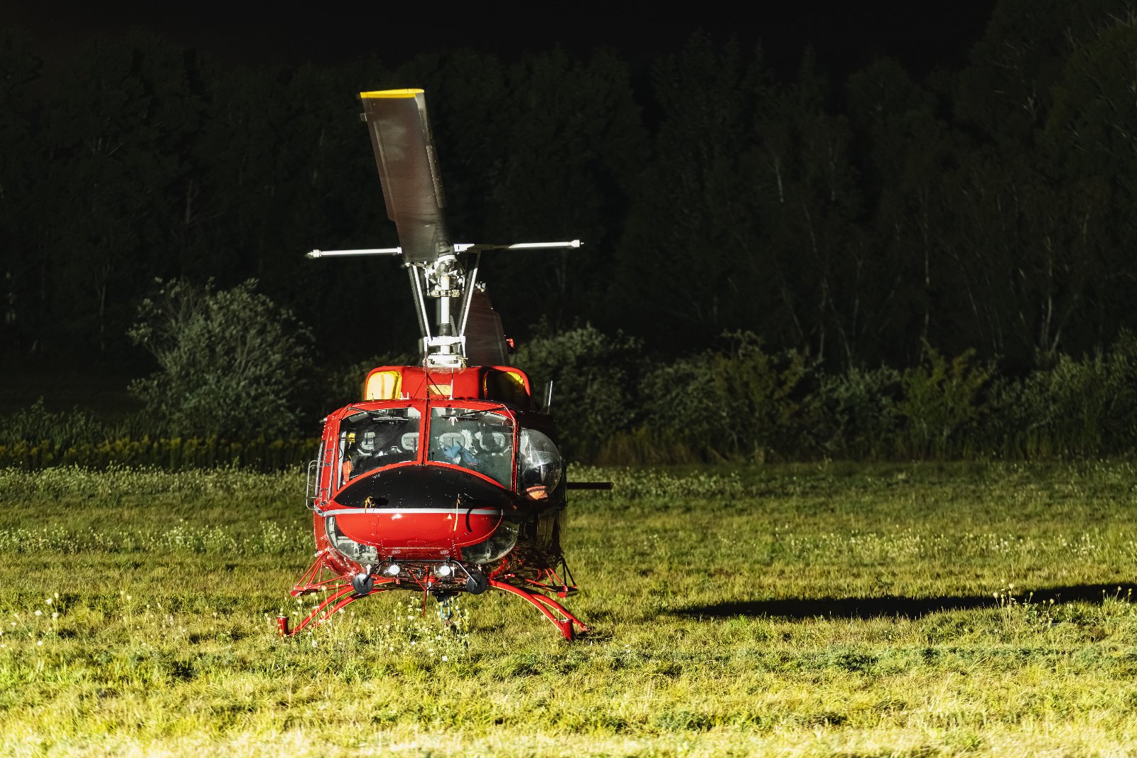 Bell 212 twin-engine helicopter landing in a field at night with landing lights on