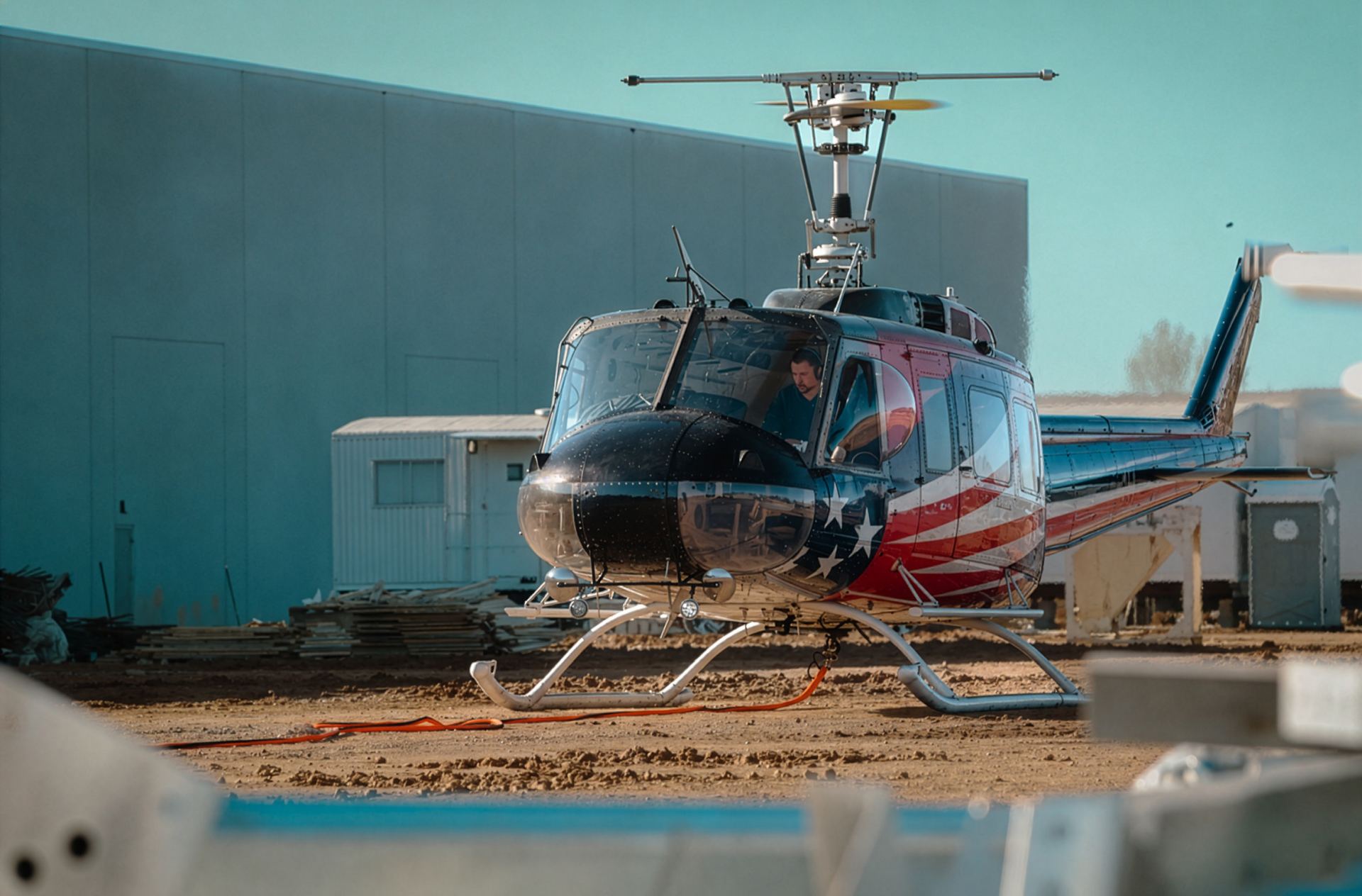 Utility helicopter parked on a dirt staging yard with ground support equipment during forward operations