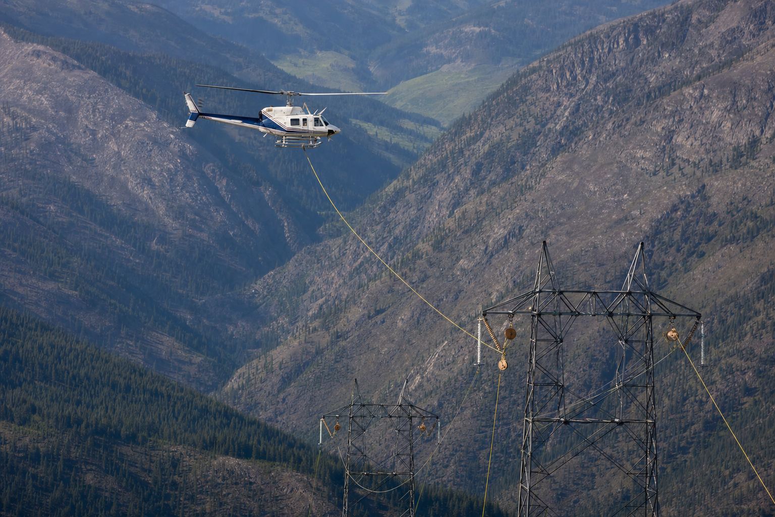 Utility helicopter flying a transmission corridor while pulling a lightweight pilot line through stringing blocks hung on lattice tower arms