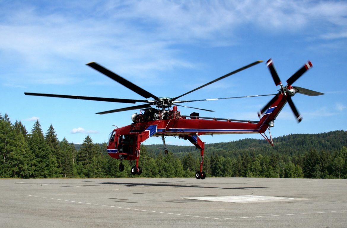 Erickson S-64 Air Crane lifting from a forest landing with timbered ridges behind