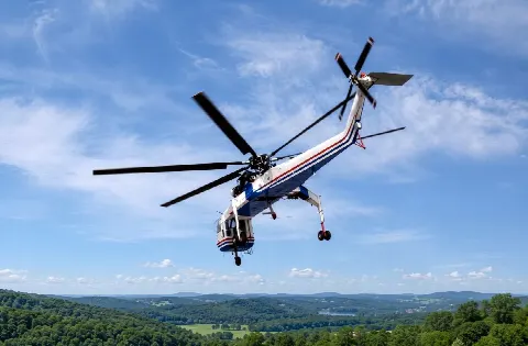 Helicopter carrying timber over forested terrain