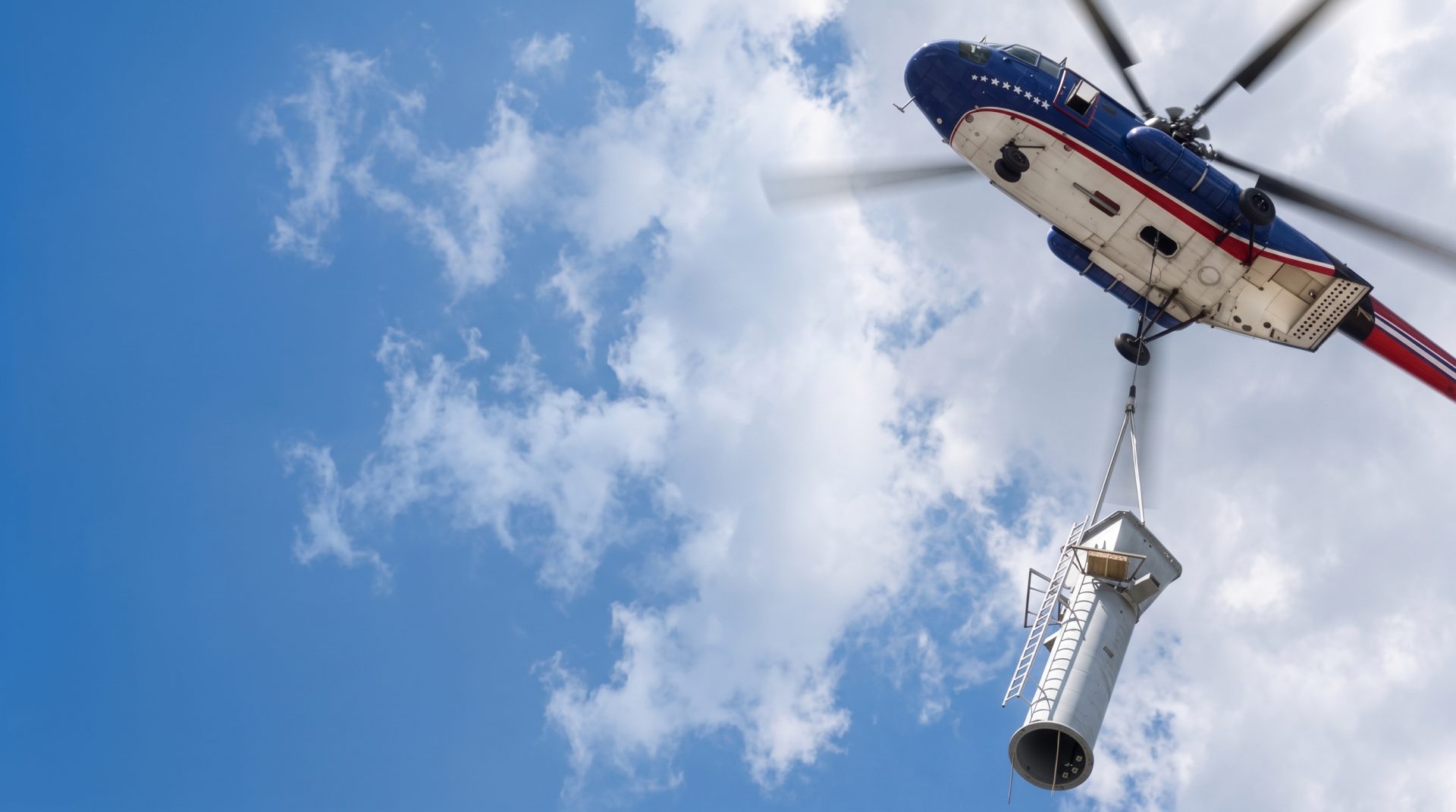 Large helicopter carrying a cylindrical industrial duct section on a longline