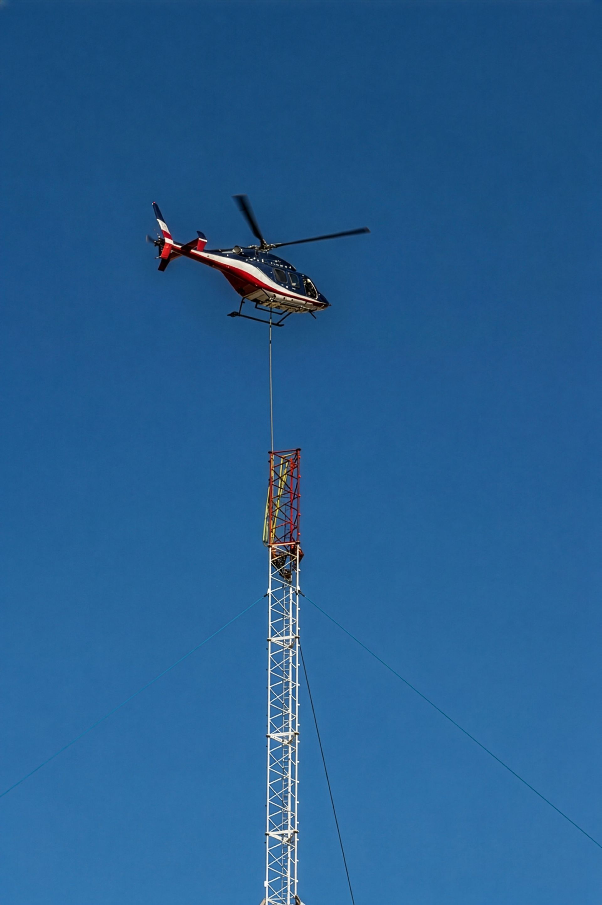Helicopter longlining a lattice tower section with riggers waiting on the structure below