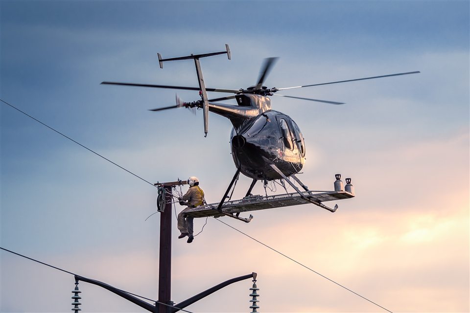 Helicopter and lineman working from a platform beside a utility pole
