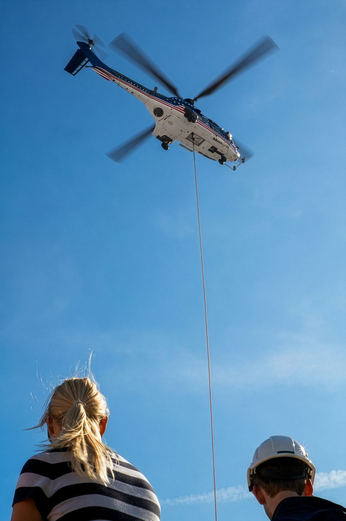 Ground crew looking up at a heavy twin helicopter hovering overhead with a longline during an external load operation