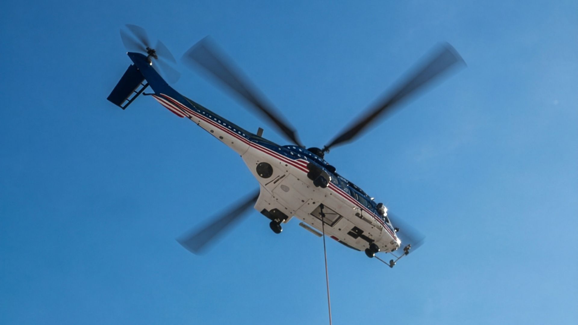 Twin-engine helicopter overhead with a longline during a utility tower lift